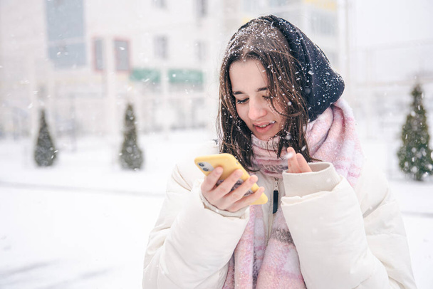 Portrait of a teenage girl outdoors with a smartphone in snowy winter weather. - Zdjęcie, obraz