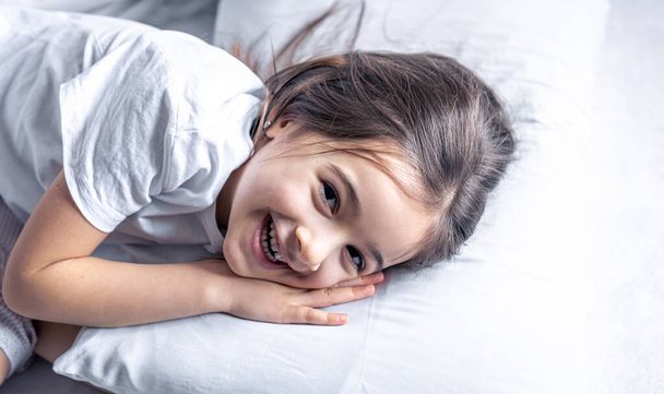 Ένα χαριτωμένο κοριτσάκι ξαπλώνει στο κρεβάτι και δεν θέλει να σηκωθεί.. - Φωτογραφία, εικόνα