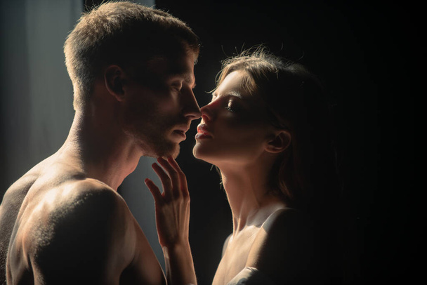 Красивая любящая пара позирует на тёмном фоне с ночным освещением. Мужчина обнимает и целует чувственную женщину. Любящая пара целуется на черном фоне. - Фото, изображение
