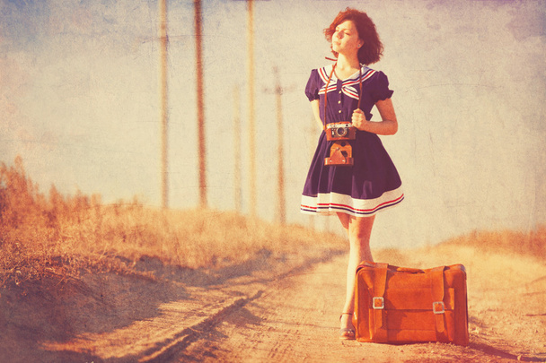 piękna brunetka dziewczyna z walizką na drodze wsi. - Zdjęcie, obraz
