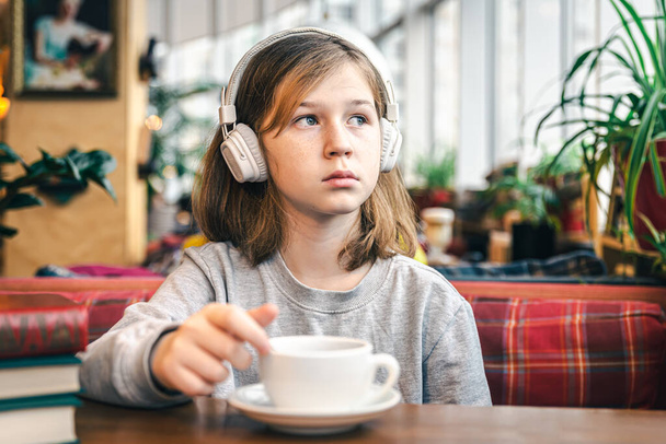 A little girl in headphones in a cafe with a cup of tea. - Valokuva, kuva