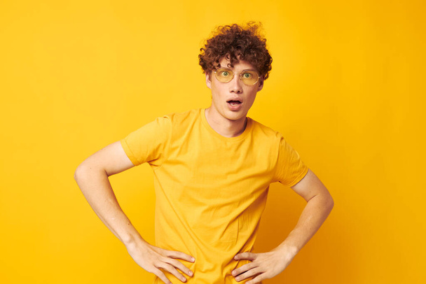 portrait of a young curly man wearing stylish glasses yellow t-shirt posing yellow background unaltered - Fotó, kép