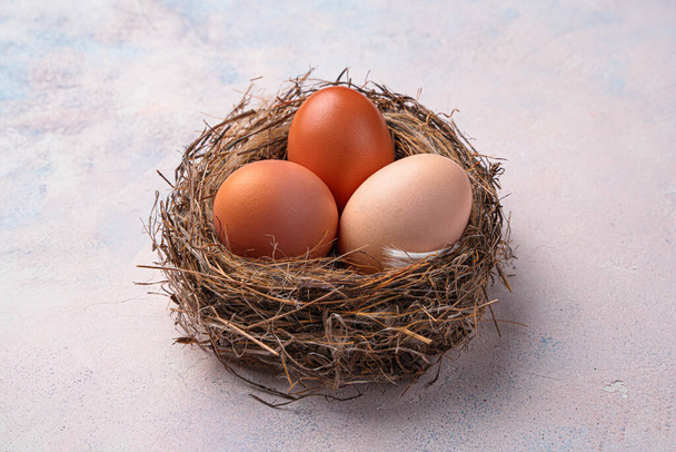 Τρία αυγά κότας σε μια φωλιά σε ελαφρύ φόντο. Κάτοψη, κοντινό πλάνο. - Φωτογραφία, εικόνα
