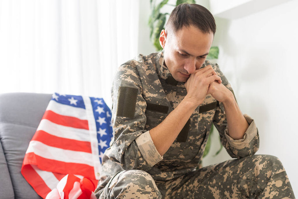 Печальный солдат в камуфляжной форме держит военную метку в сжатых руках - Фото, изображение