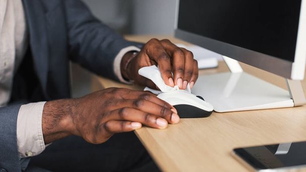 Unrecognizable black office worker wiping computer mouse with disinfectant at desk, closeup - Photo, image