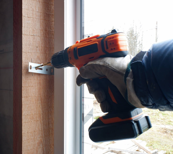 installatie van kunststof in een frame huis, de bouwer schroeven het raamkozijn aan de hellingen met een schroevendraaier. close-up. - Foto, afbeelding