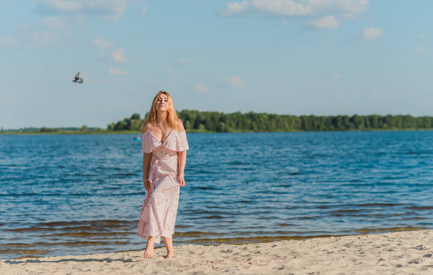 Plajda pembe romantik, yumuşak, uzun elbiseli bir kadın, güneşli sıcak bir gün. Rahatla ve özgürlük kavramı  - Fotoğraf, Görsel