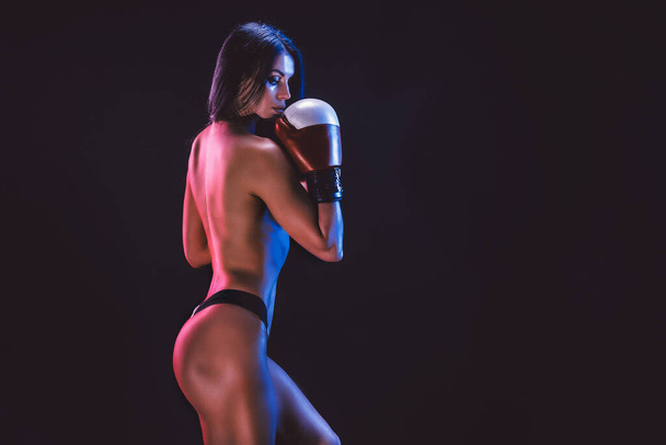 erotic studio shot of young brunette athlete woman in boxing gloves who stands on black background - Фото, изображение