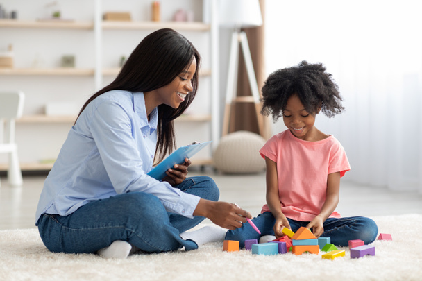Liebenswertes schwarzes Kind und Kinderpsychotherapeut spielen mit Ziegeln - Foto, Bild