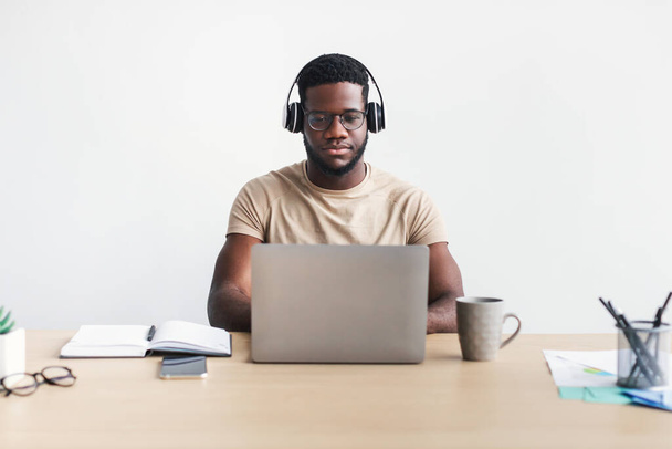 Enfocado joven negro chico en los auriculares de chat en línea, tener reunión de negocios en el ordenador portátil en la mesa - Foto, Imagen
