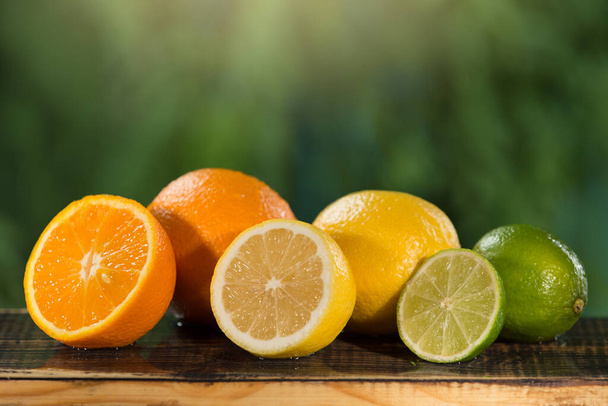 citrus fruits lie on wooden boards, on a background of greenery, part of the fruit is cut, concept, copy space - Foto, imagen
