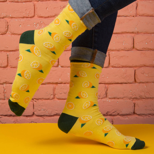 female legs in yellow socks with drawings of lemon, on a yellow surface, concept, on brick wall background - Valokuva, kuva