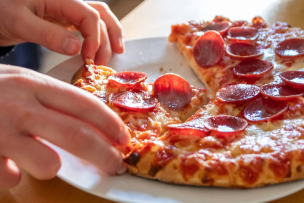 ホットスチームとおいしいチーズのピザサラミの子供の手を保持する部分は、マクロビューで喜びを食べる食事のためのカロリーと不健康なスナックとしてクローズアップショットファーストフードの食事 - 写真・画像