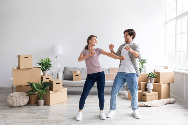 Glad happy european millennial guy and female have fun dancing together in room interior among boxes - Foto, Imagen