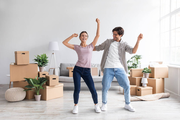 Smiling caucasian millennial woman and man dance together, have fun in room interior among boxes - Photo, Image