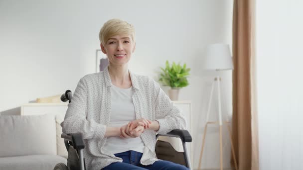 Keski-ikäinen vammainen nainen istuu pyörätuolissa ja hymyilee kameralle, poseeraa kotona sisustus, zoomaa muotokuva - Materiaali, video