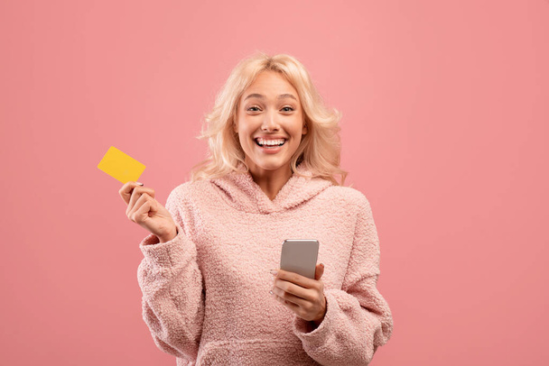 Liikkuva pankki. Innoissaan nainen tilalla älypuhelin ja luottokortti, käyttämällä sovellusta sähköisen kaupankäynnin tai ostoksia verkossa - Valokuva, kuva