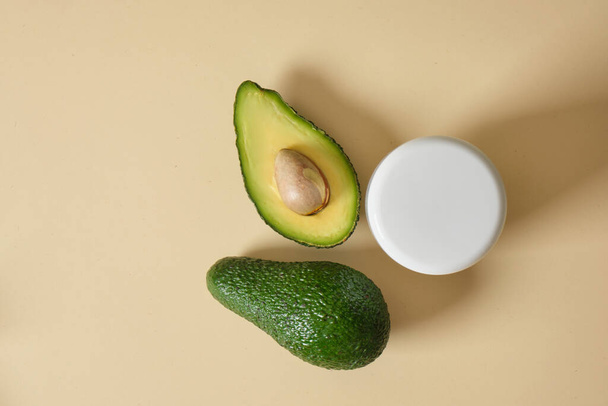 white mock-up cosmetics jar and avocado on a beige background, skin care with natural cosmetics, masks and creams with avocado oil copy space top view - Fotografie, Obrázek