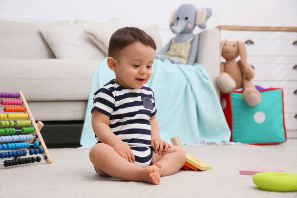 Cute baby boy playing with toys on floor at home - Fotó, kép
