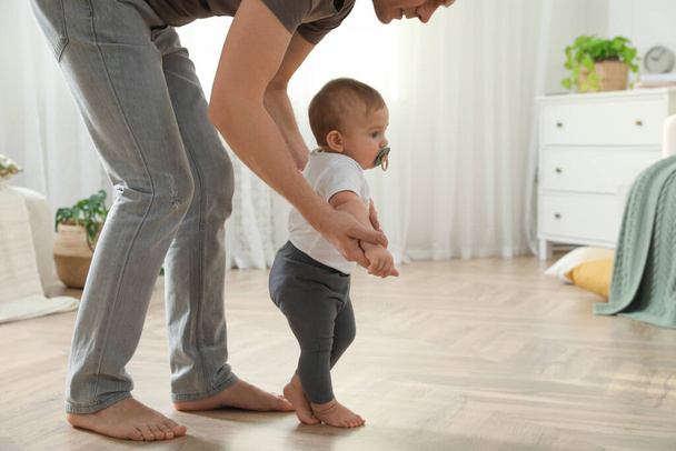Father supporting his baby daughter while she learning to walk at home - Φωτογραφία, εικόνα
