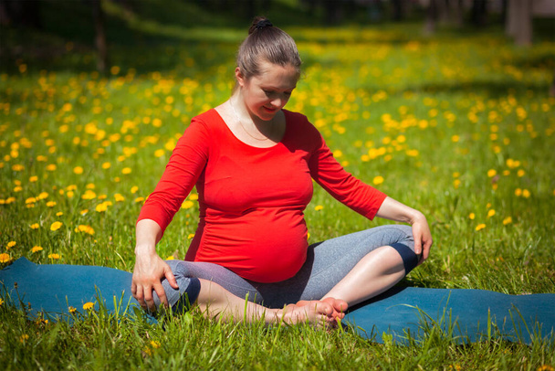 Ejercicio de yoga en el embarazo - mujer embarazada haciendo asana baddha konasana ángulo limitado pose al aire libre en césped de hierba con dientes de león en verano - Foto, Imagen