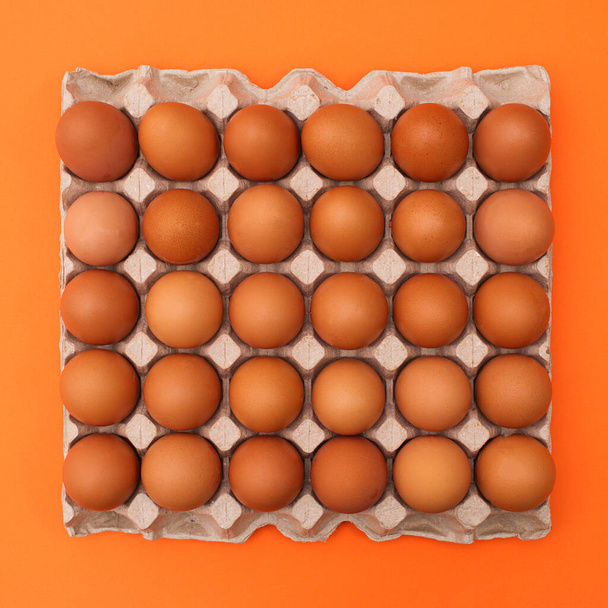 Cardboard box with eggs on vibrant orange background. Easter food. Flat lay - Foto, Imagen