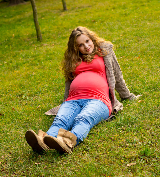 Beautiful pregnant blonde lying on green grass. Portrait of pregnant woman. Outdoors - Photo, Image