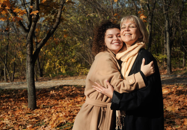 Middle aged woman and young curly hair woman walking in autumn park.Mother and daughter relationship - Photo, Image