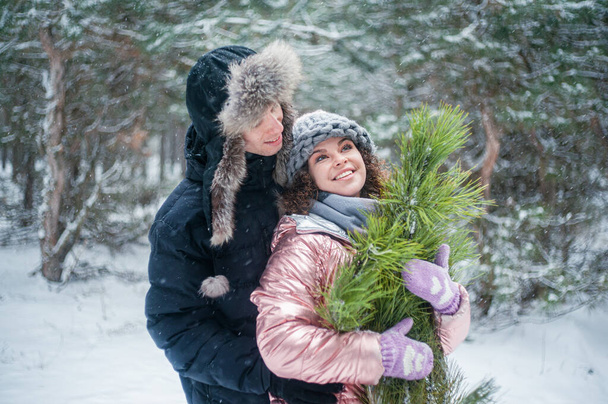 Woman and man walking in winter forest. Happy couple holding pine tree has fun with snow. - Photo, Image