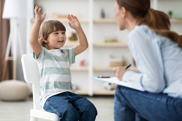 Happy emotional little boy talking to therapist at office, sharing funny story to specialist during session - Фото, зображення