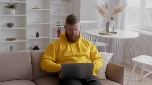Homme freelance à l'aide d'un ordinateur portable travaillant en ligne assis sur le canapé à l'intérieur - Séquence, vidéo