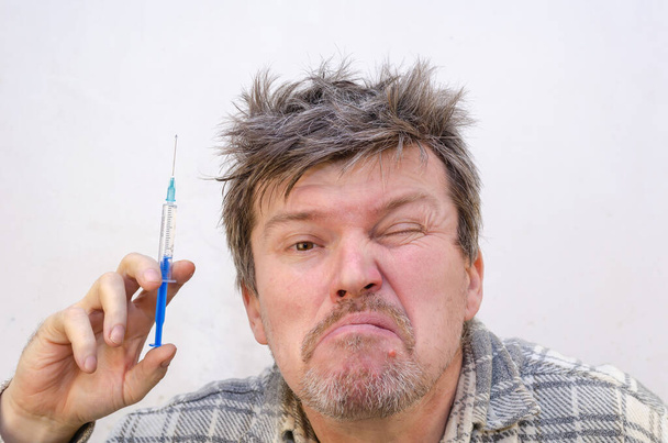 Dospělý muž s rozcuchanými vlasy drží v ruce stříkačku. Injekční stříkačka je naplněna čirou tekutinou. - Fotografie, Obrázek