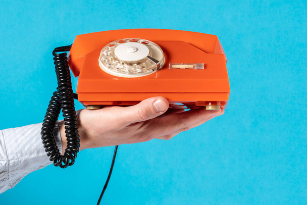 Hand mit altem Drehtelefon über blauem Hintergrund. Kommunikationskonzept. - Foto, Bild