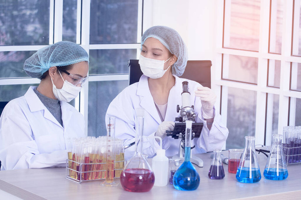 Laboratoire deux femmes scientifiques Mener des expériences. Le chercheur scientifique en chef ajuste le spécimen dans un plat de Petri et le regarde au microscope. - Photo, image
