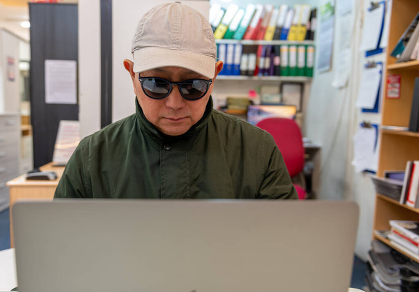 Un uomo che usa un portatile online indossando occhiali da sole e un cappello. Criminalità informatica, sicurezza, truffe finanziarie concetto. - Foto, immagini