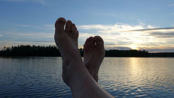 Füße auf dem Boot bei Sonnenuntergang gekreuzt - Foto, Bild