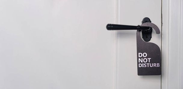Niet storen tekstbord, hotel kamer hanger. Zwart etiket op gesloten deurkruk met retro panelen, close-upweergave. Witte houten deur - Foto, afbeelding