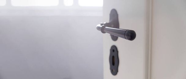 Открыть люк. Ретро черная металлическая дверная ручка и ключ-замок на белой деревянной двери, размывают интерьер комнаты. Баннер, копировальное пространство - Фото, изображение