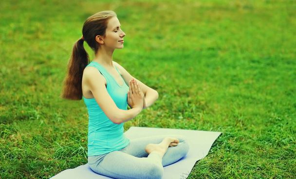 Young woman doing yoga exercises on a mat on the grass in summer park - Φωτογραφία, εικόνα