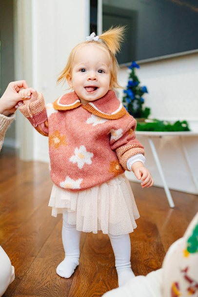 cute little girl in a pink sweater with flowers holds moms hand. first steps - Foto, Imagen