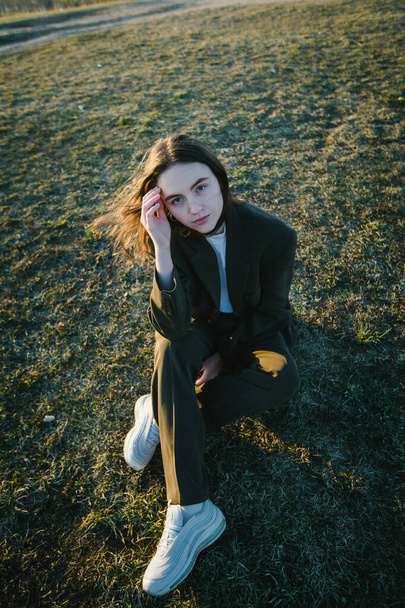 Une jolie fille dans une veste est assise sur l'herbe à l'extérieur. - Photo, image