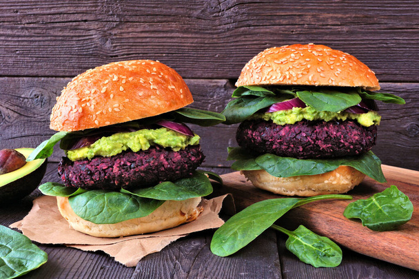 Vegetarian beet burgers with avocado and spinach. Side view table scene against a rustic dark wood background. - Photo, Image