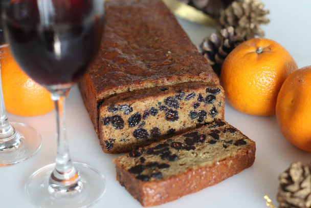 Slices of boiled fruit cake. An easy fruit cake with no alcohol. Made using dry fruits boiled in orange juice. Shot on white background along with red wine and oranges. - Photo, Image
