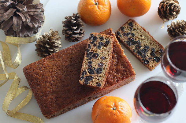 Slices of boiled fruit cake. An easy fruit cake with no alcohol. Made using dry fruits boiled in orange juice. Shot on white background along with red wine and oranges. - Photo, Image