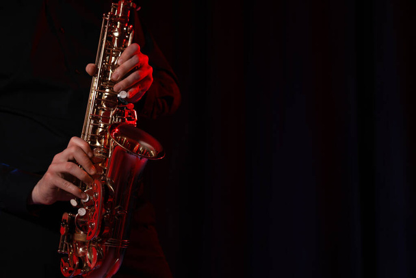 Man with saxophone on dark background, closeup. Space for text - Fotó, kép
