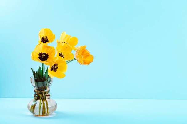 Großer Blumenstrauß aus gelben Tulpen in Vintage-Glasvase auf blauem Hintergrund. Kopierraum. Visitenkarte. Einladungskarte. Grußtext Ort. Internationale Feiertage. Banner. Hallo Frühling. - Foto, Bild