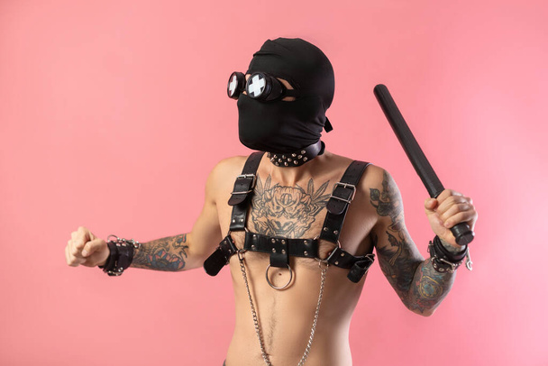 Балаклава чоловік зі шкіряними ремінцями на тілі для бдсм секс-іграшок з гумовою паличкою в руках
 - Фото, зображення