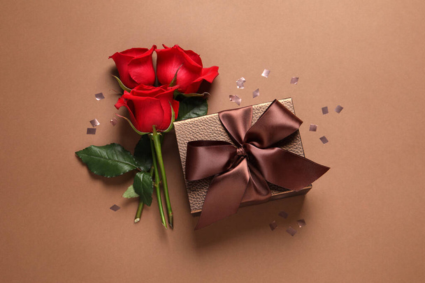 Bela caixa de presente, flores e confetes em fundo marrom, flat lay - Foto, Imagem