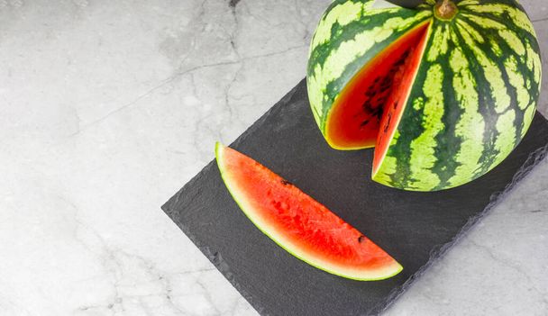 Healthy food concept. A piece of ripe fresh watermelon with a knife on a slate board on a light background. Vegetarian food. Copy space - Fotografie, Obrázek