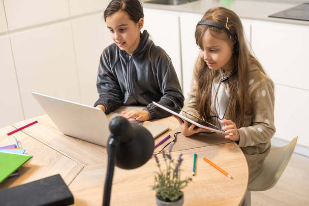 Online training. Twee schoolmeisjes met koptelefoon luisteren naar lessen op laptops. School thuis in een pandemie en quarantaine. - Foto, afbeelding